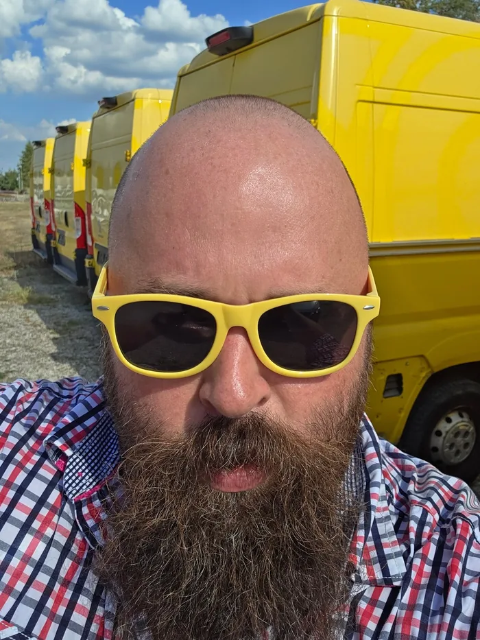Gert Bauer mit gelber Sonnenbrille vor einer Reihe gelber Transporter